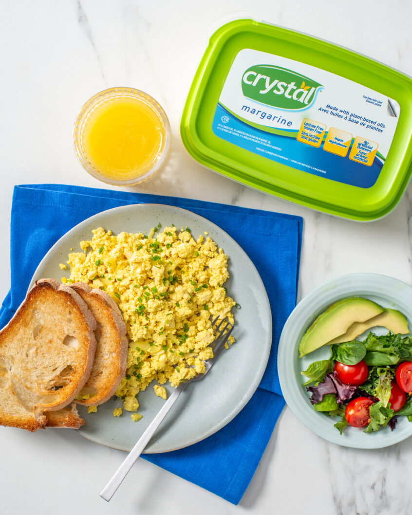 Power-packed tofu scramble on a plate with 2 pieces of bread. Next to it there is a juice and Crystal margarine package.